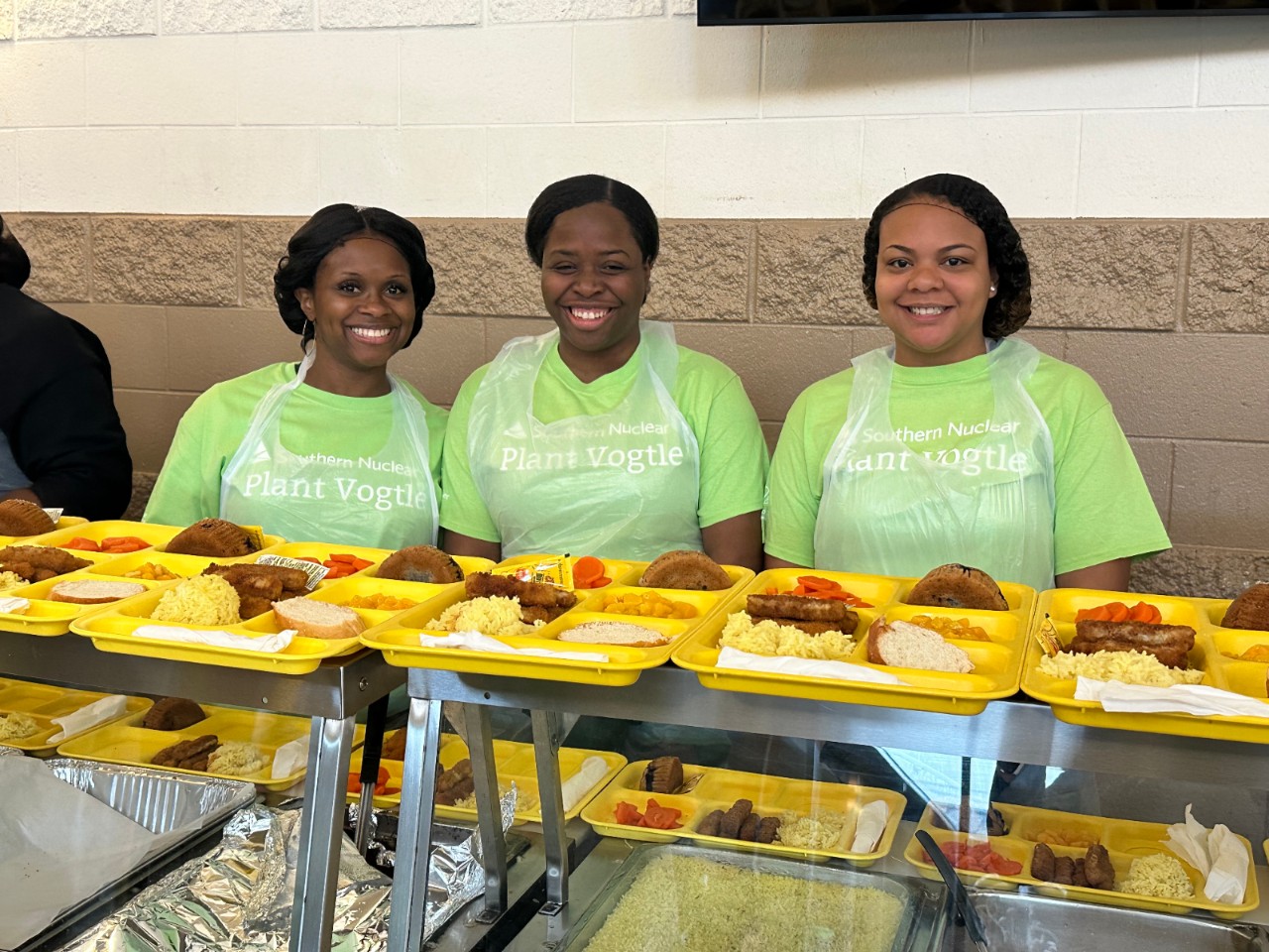Smiling Southern Nuclear employees at Plant Vogtle serve school lunches, demonstrating care and presence in the nuclear community.