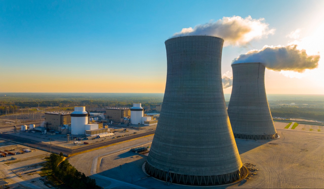 Two massive cooling towers release steam at Southern Nuclear's Plant Vogtle with nearby facilities and forested surroundings.