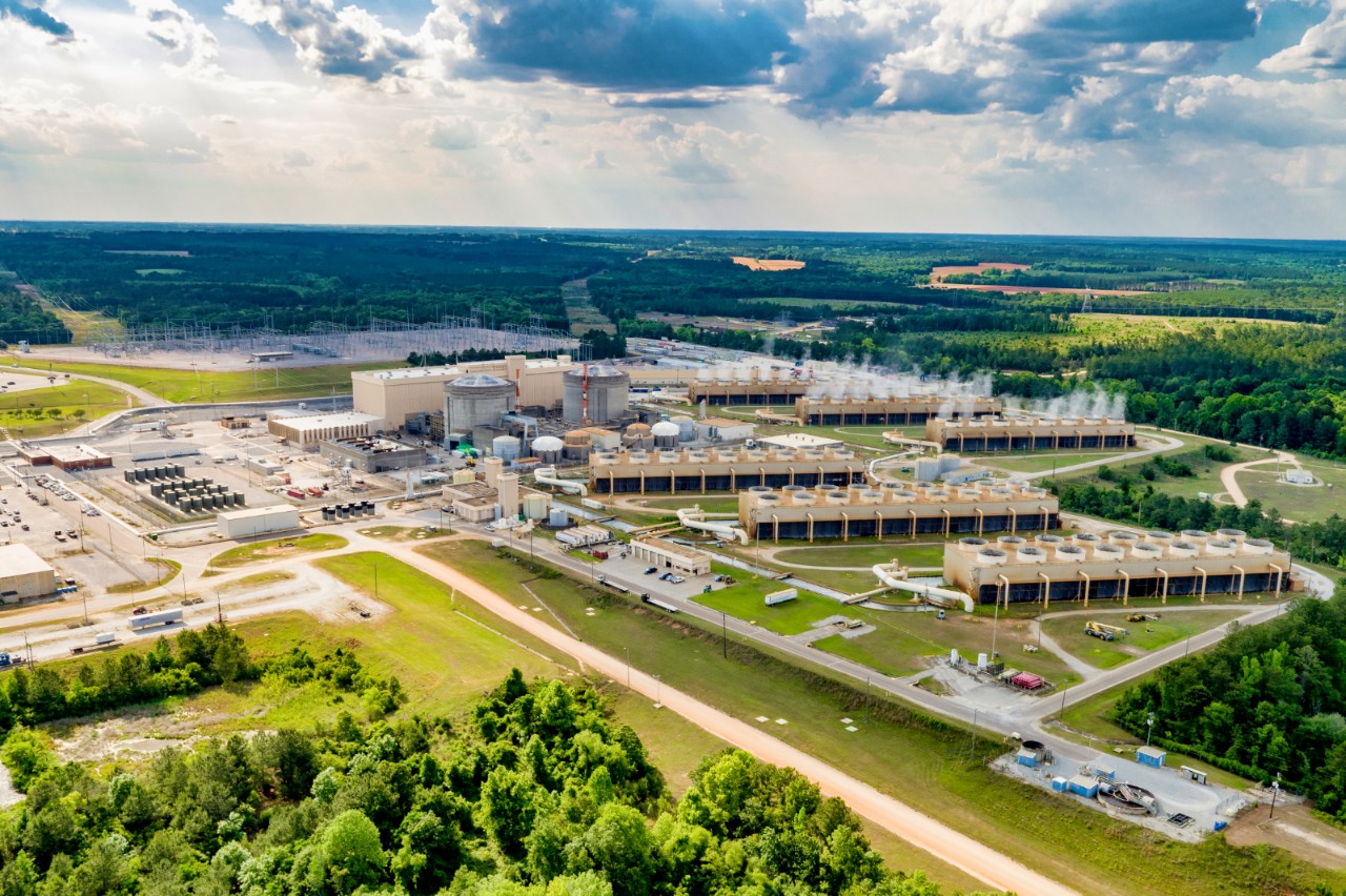 Aerial view of Southern Nuclear's Plant Farley, with steam-rising cooling towers and industrial buildings surrounded by dense green forest.