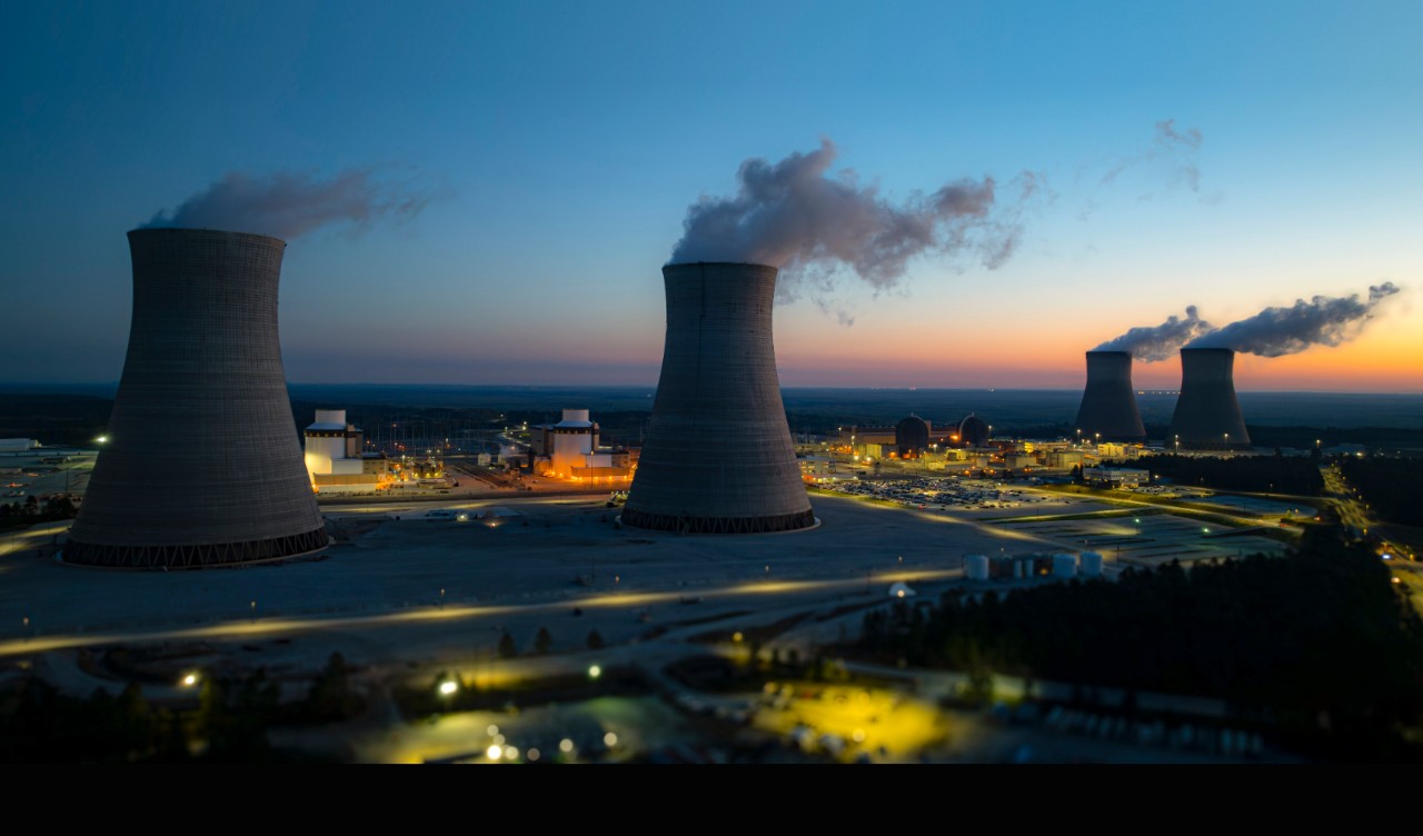 Twilight view of Vogtle Power Plant with steam rising from its cooling towers, lights glowing across the facility, and a vivid evening sky.